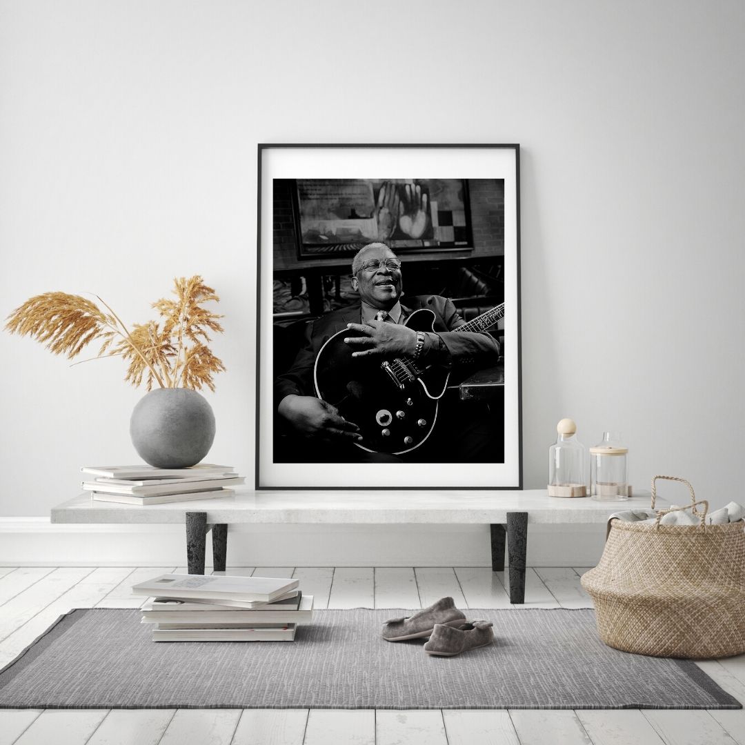 Framed black and white photograph of a musician playing guitar in a living room setting.