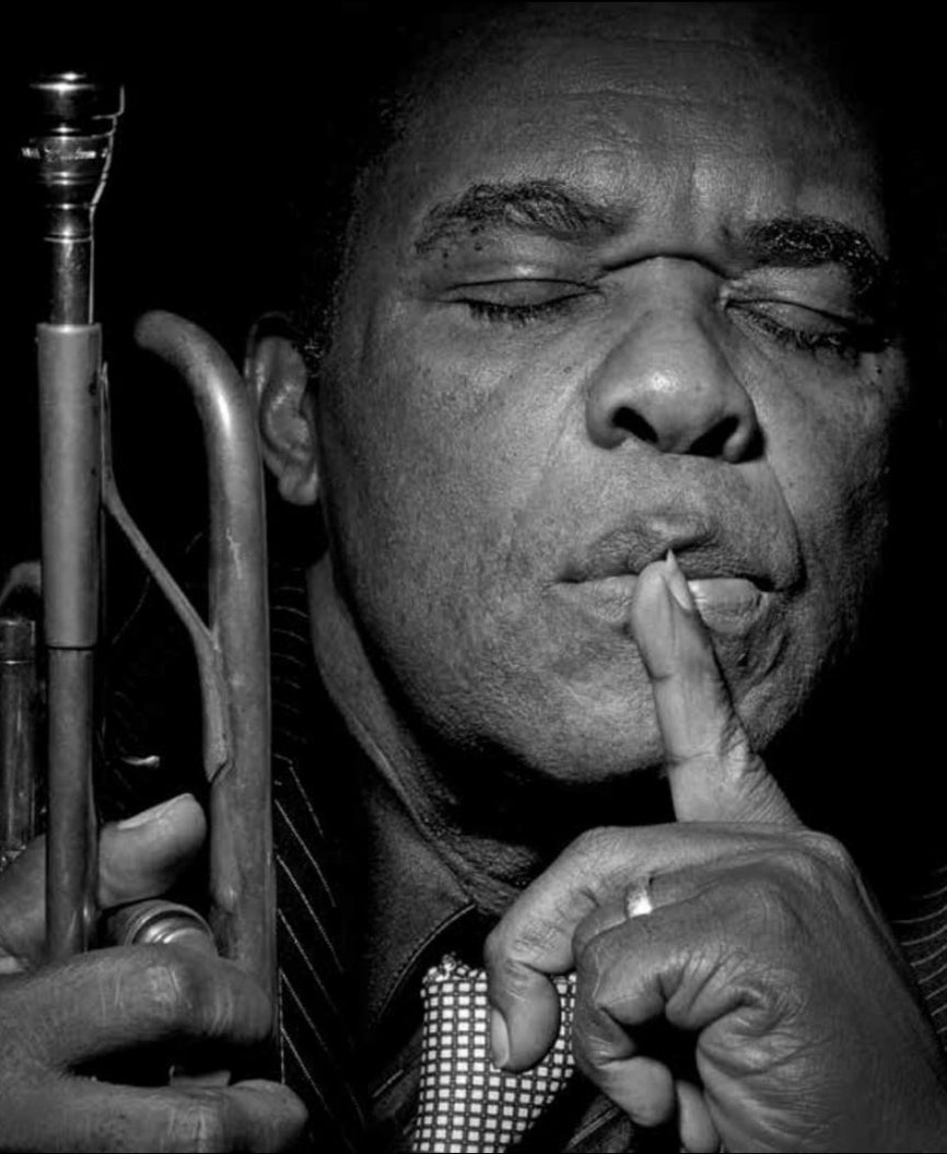 Black and white portrait of Freddie Hubbard with a trumpet and his eyes closed.