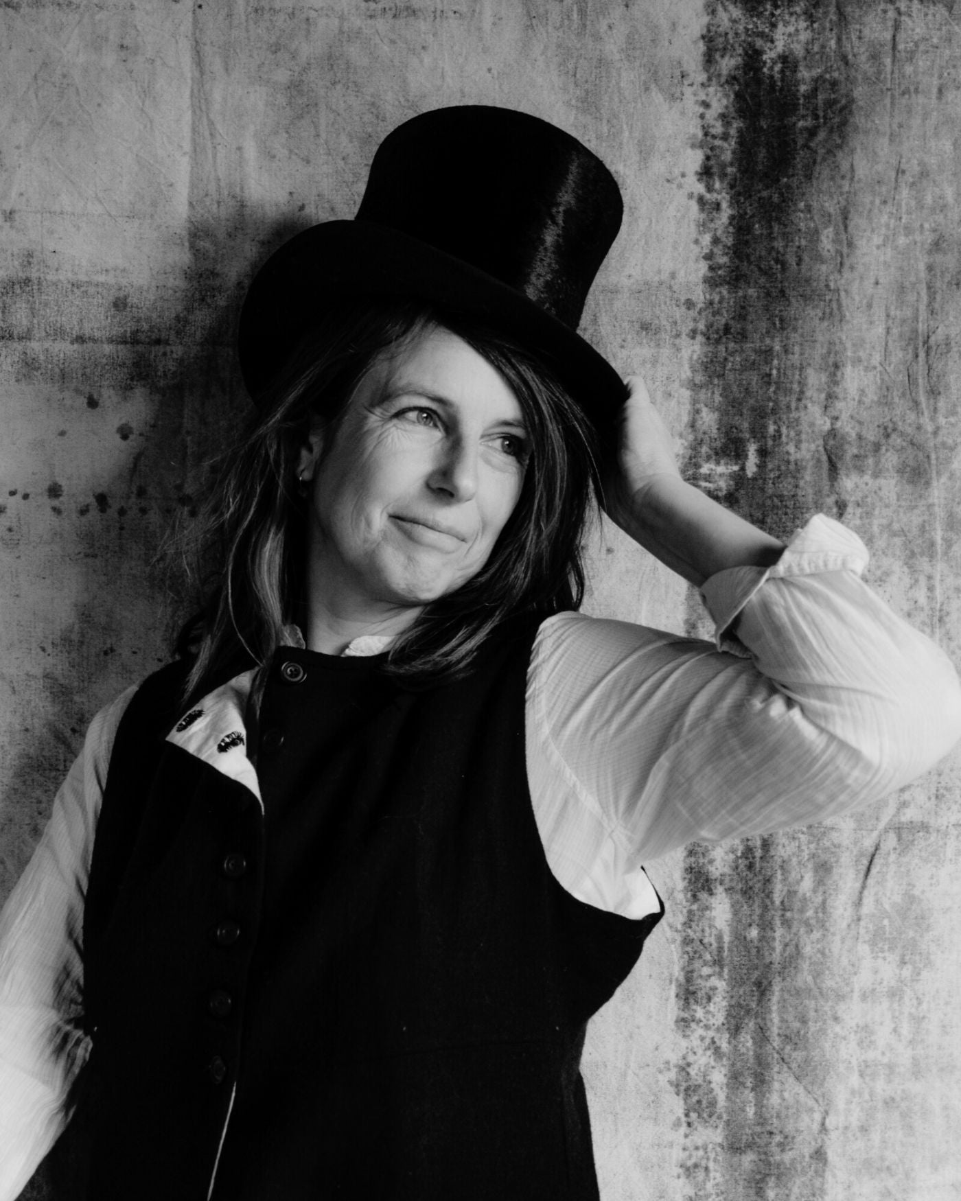 British photographer Joanna Maclennan wearing a top hat against a textured wall