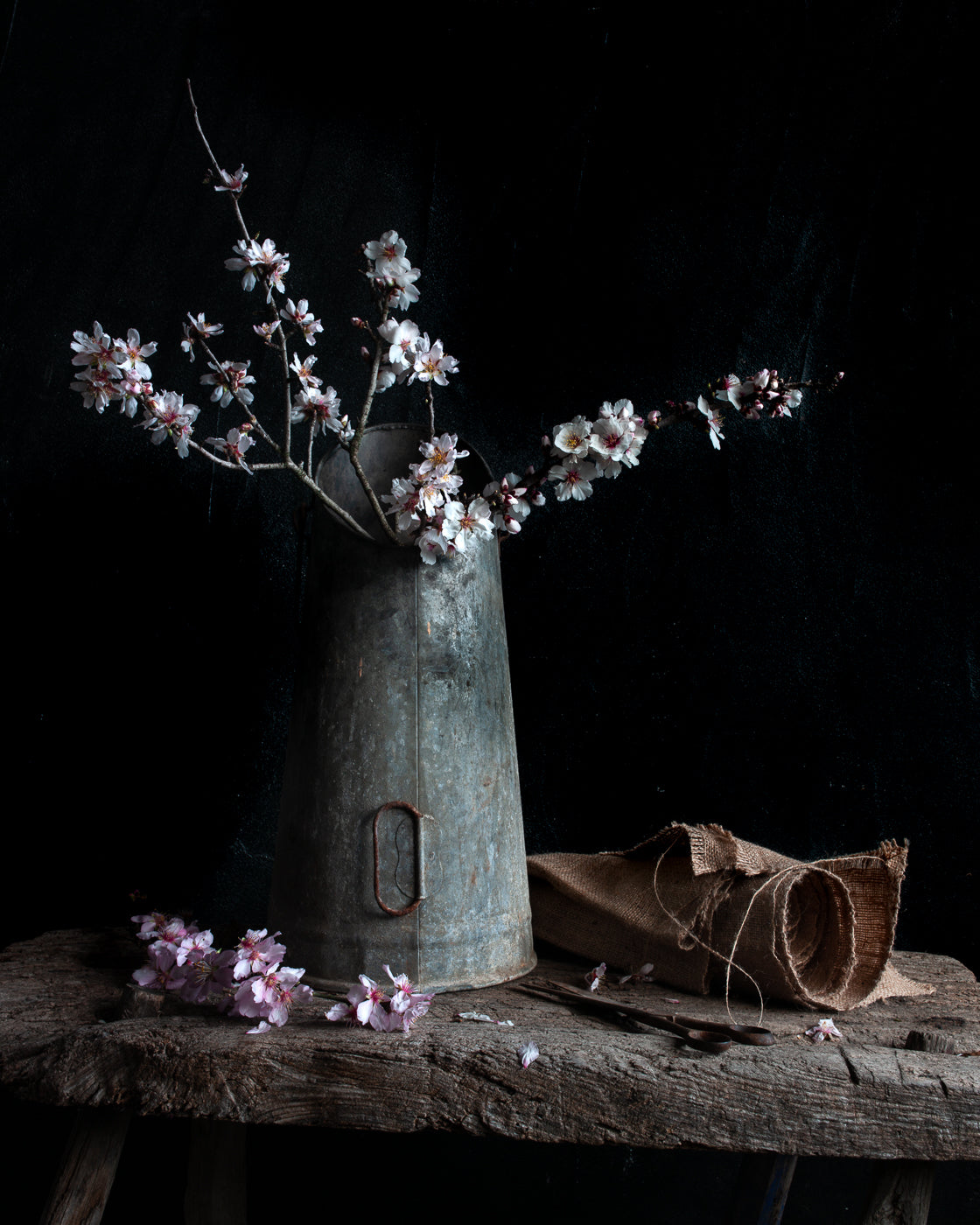 Floral arrangement in an old metal container on a wooden surface against a dark background.