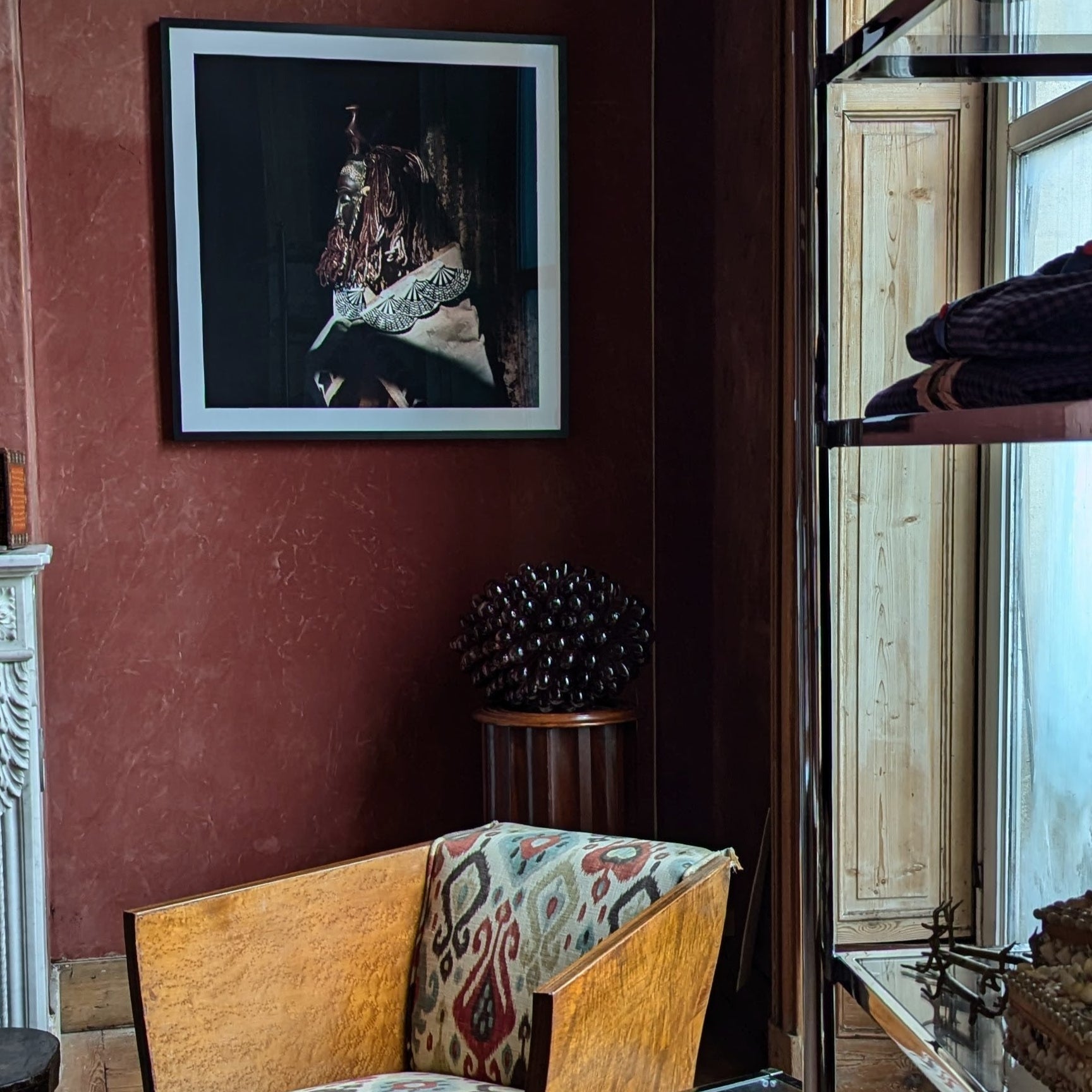 Vintage-style room with wooden armchair, framed artwork on red wall, and decorative elements.