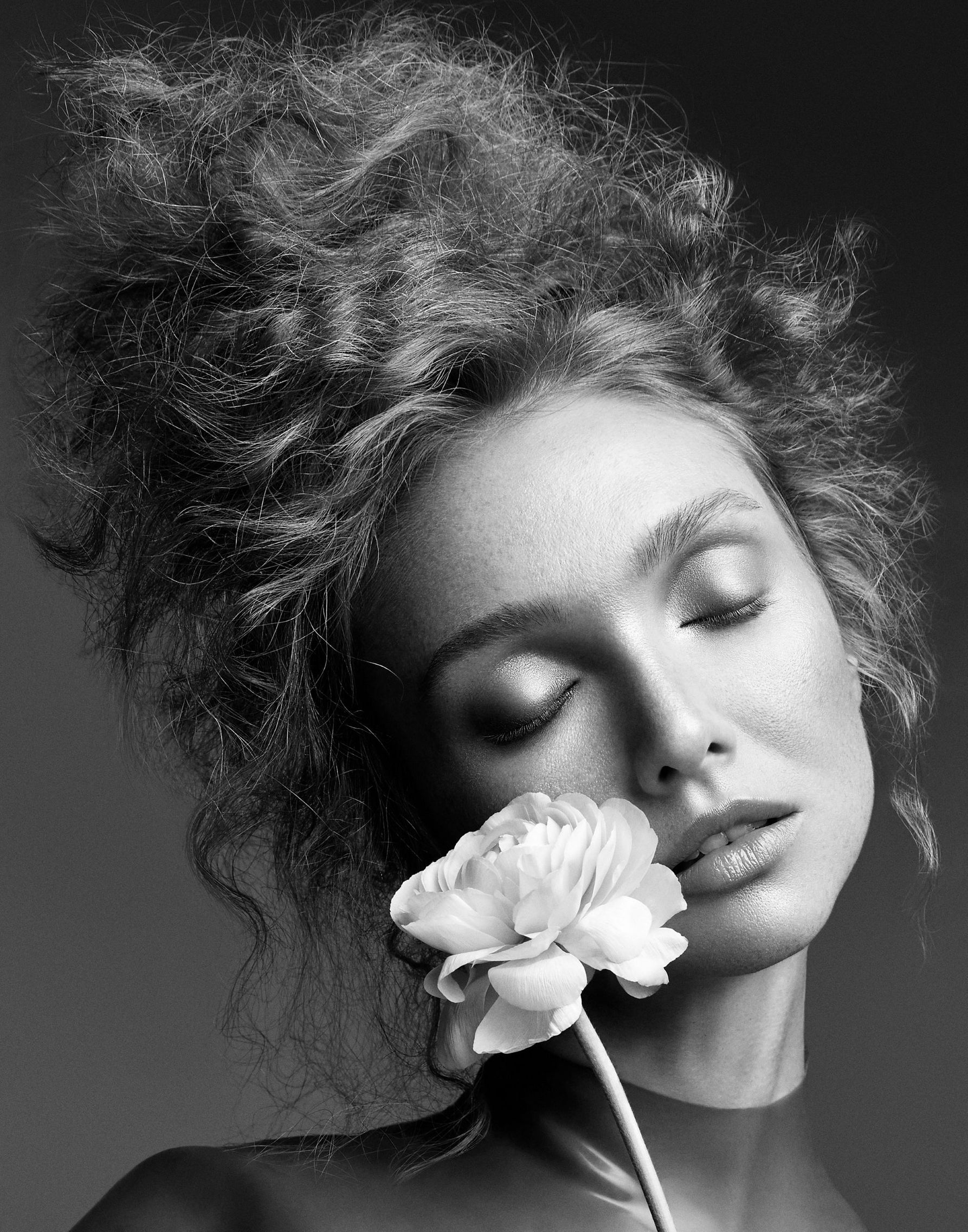 Black and white portrait of a woman with a flower near her face against a dark background