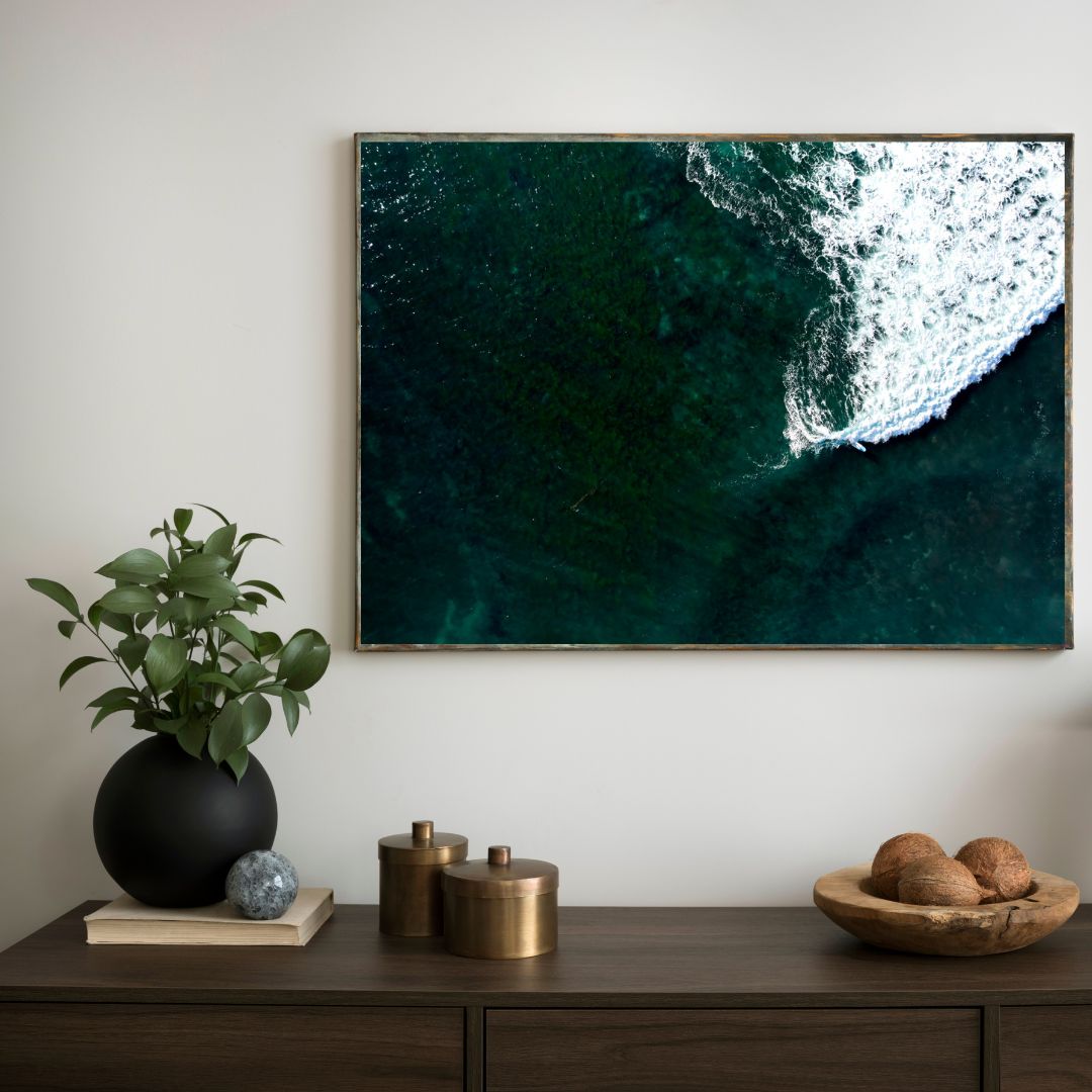 Framed artwork of ocean waves above a wooden console table with decorative items.