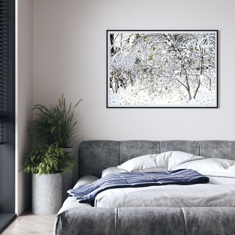 Modern bedroom with a bed, plant, and framed artwork on the wall.