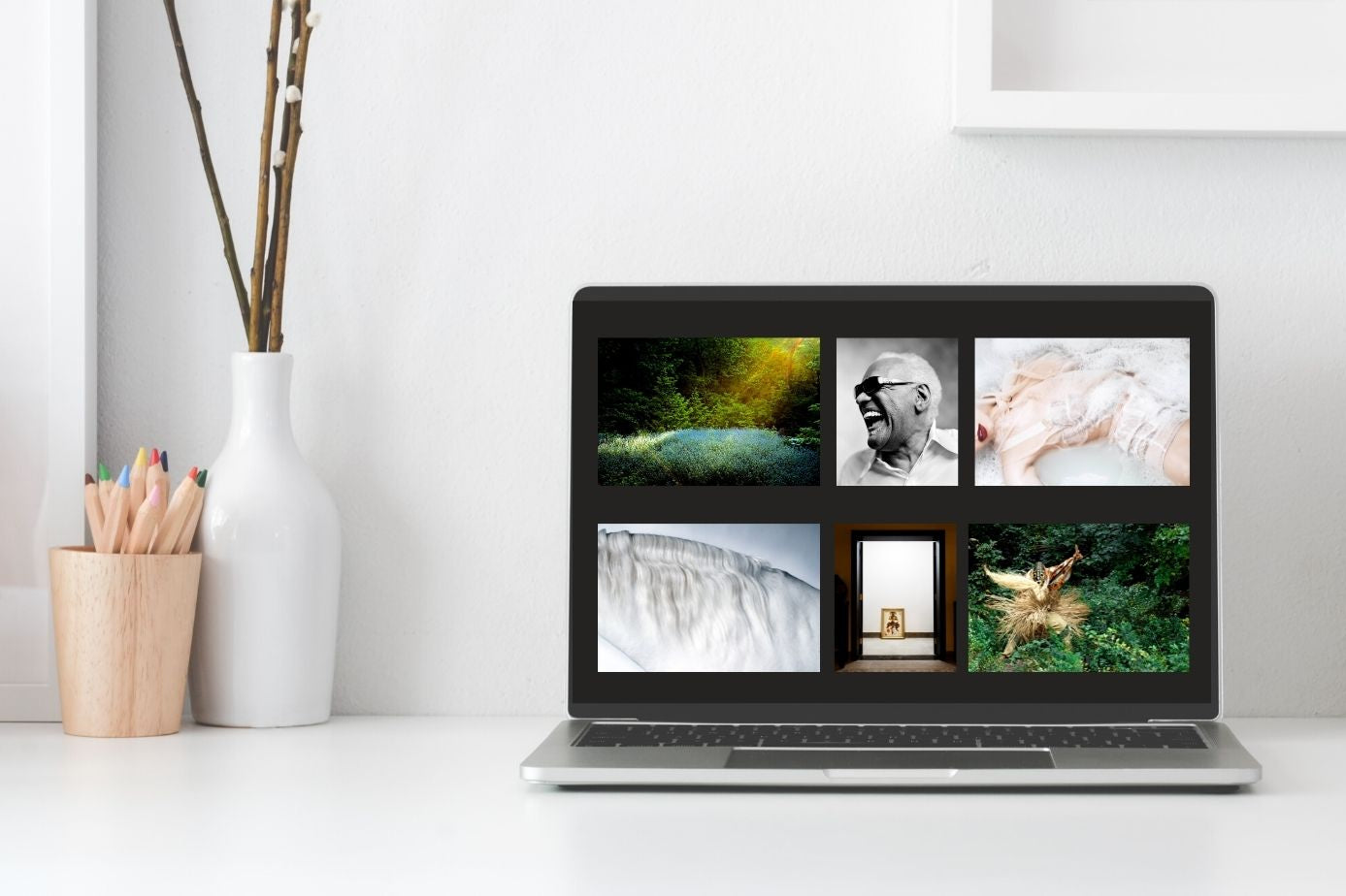 Laptop displaying a collage of images on a white desk with a vase and pencils.