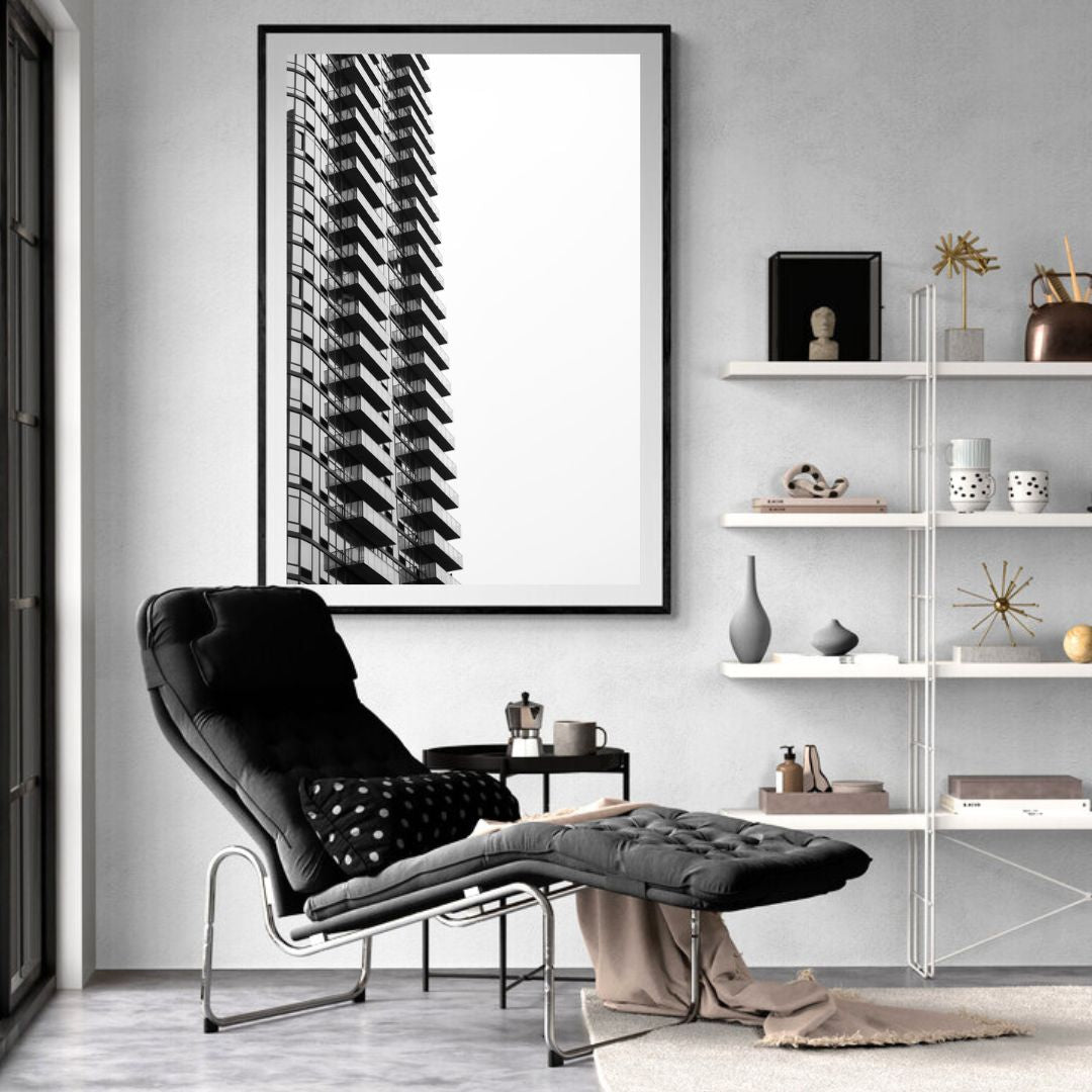 Modern living room with a black armchair, white shelves, and a framed black and white photo of a building.