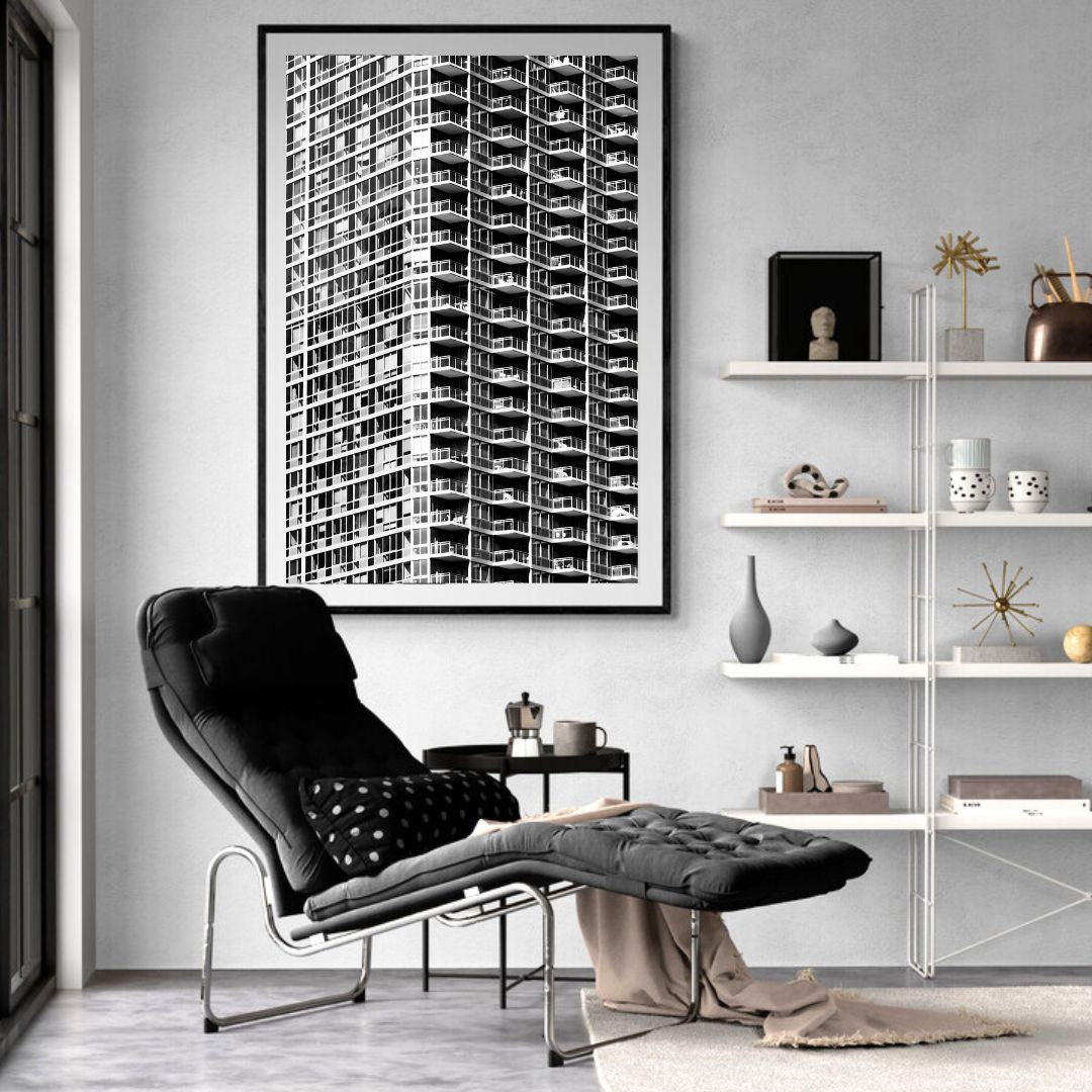 Modern living room with a black armchair, white shelves, and a large framed black and white photo of a building.