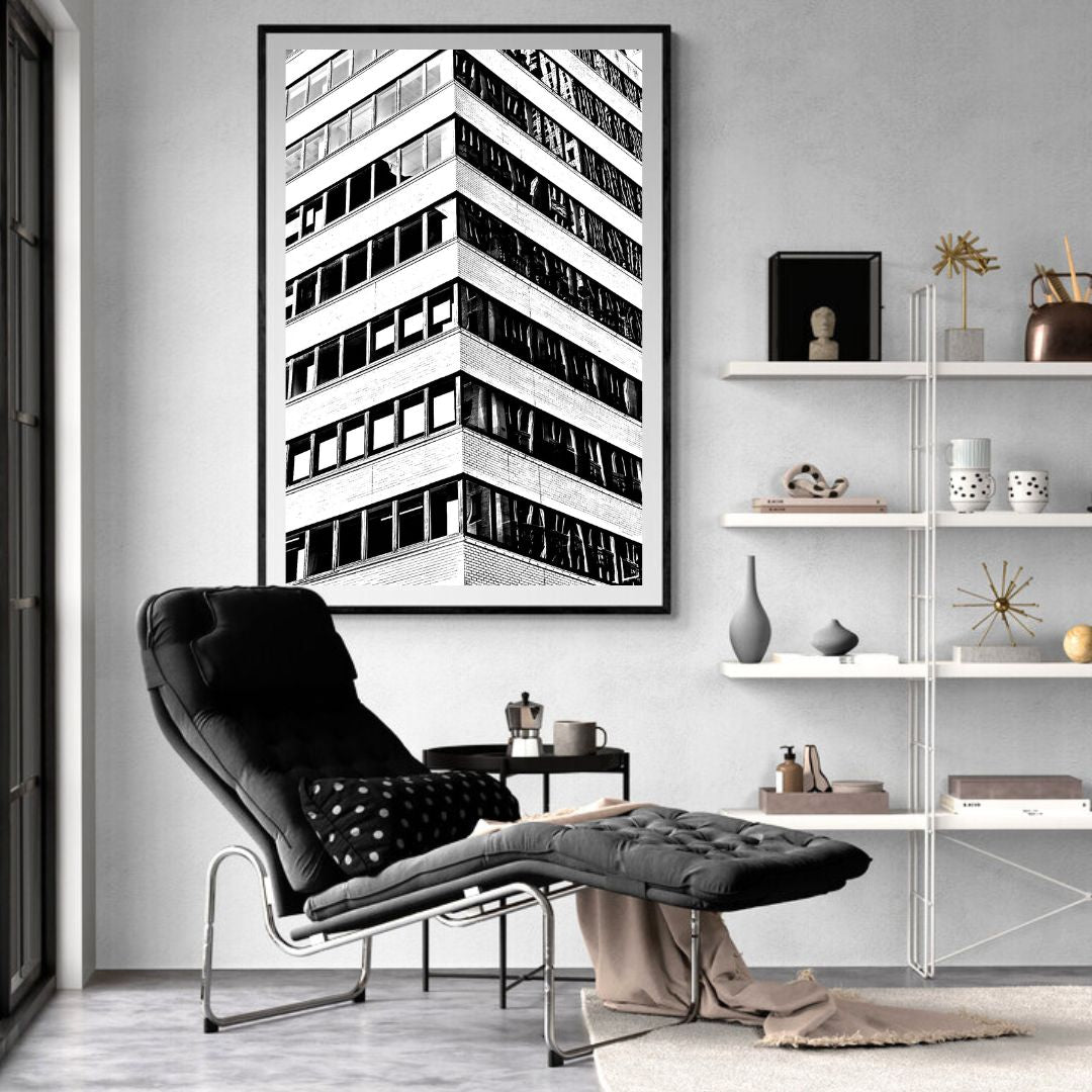 Modern interior with a black and white abstract art print of a building, a black armchair, and a white shelf.