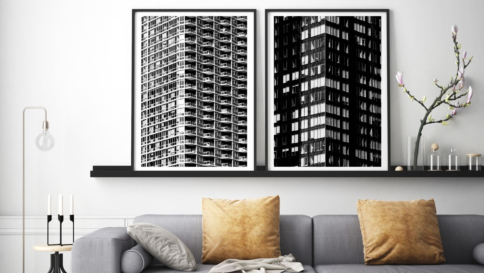 Two black and white framed artworks on a wall above a gray sofa with gold cushions.