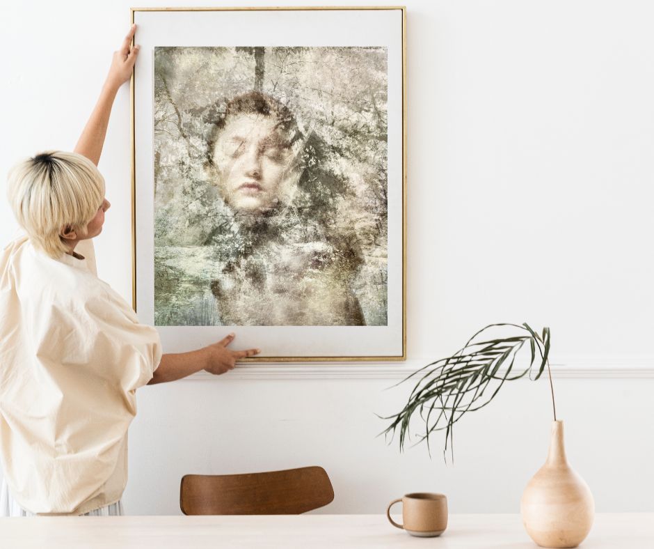 Person hanging a framed artwork of a woman on a wall.