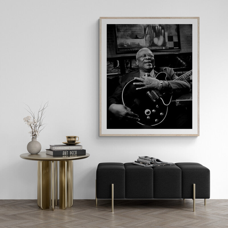 Framed black and white portrait of a musician playing guitar in a living room setting.