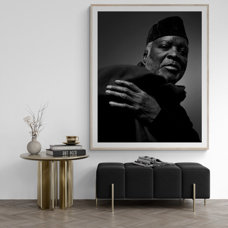 Framed black and white portrait of a man in a modern interior setting with a table and bench.