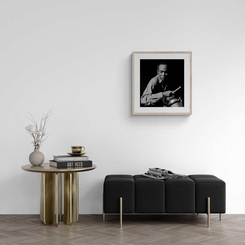Modern living room with a black sofa, round wooden table, and framed black and white portrait on the wall.