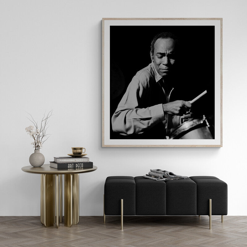 Framed black and white portrait of a man playing drums in a modern living room.