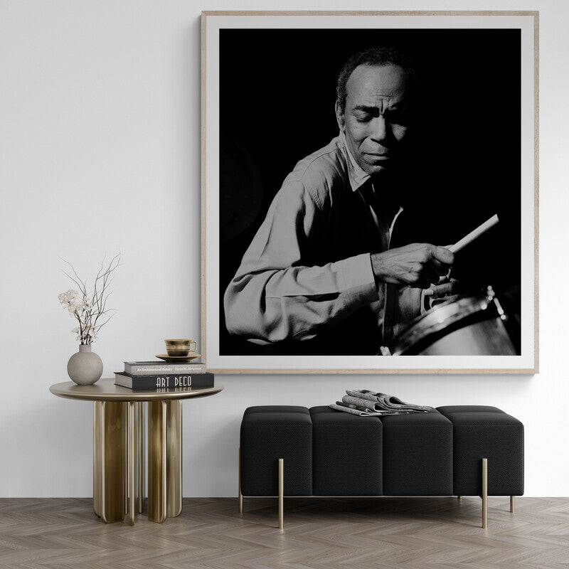 Framed black and white portrait of a man playing drums in a modern living room.