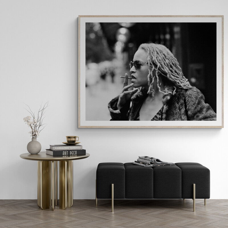 Framed black and white portrait of a person with dreadlocks smoking, above a modern living room setup.