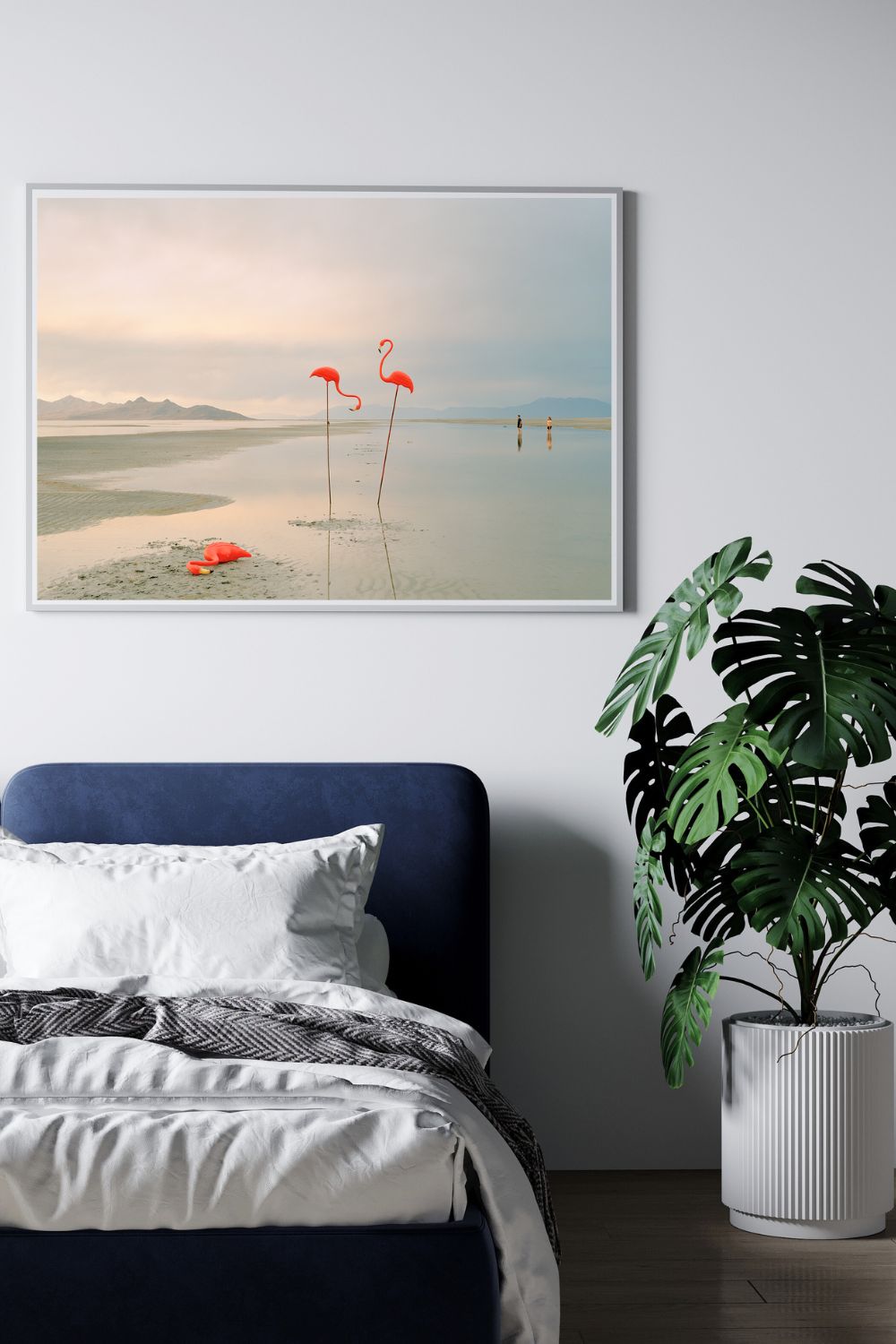 Bedroom with a framed photograph of flamingoes on the wall, a plant, and a bed.