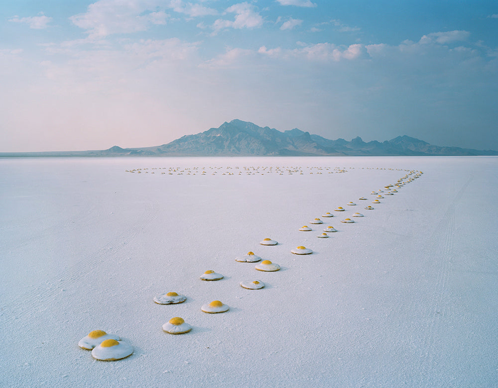 Row of plastic eggs on a vast, flat salt flat with mountains in the distance.