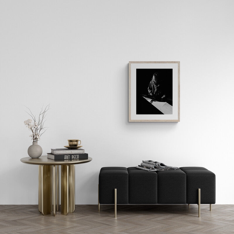 Modern living room with a black sofa, round wooden table, and framed artwork on the wall.