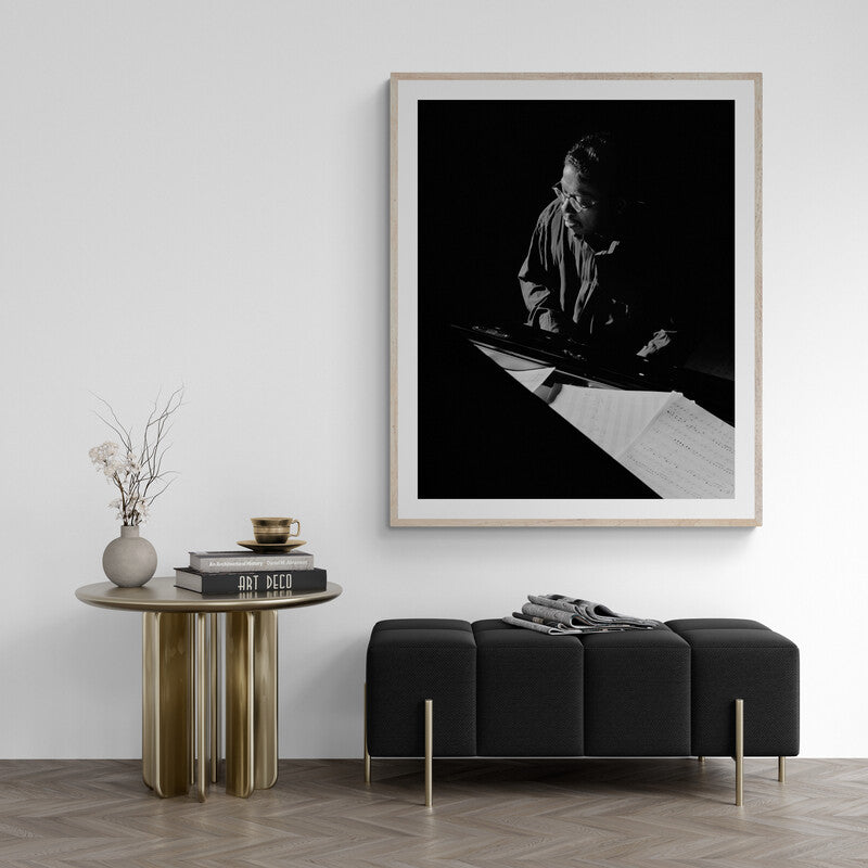 Framed black and white artwork of a person sitting on a bench in a minimalistic room.