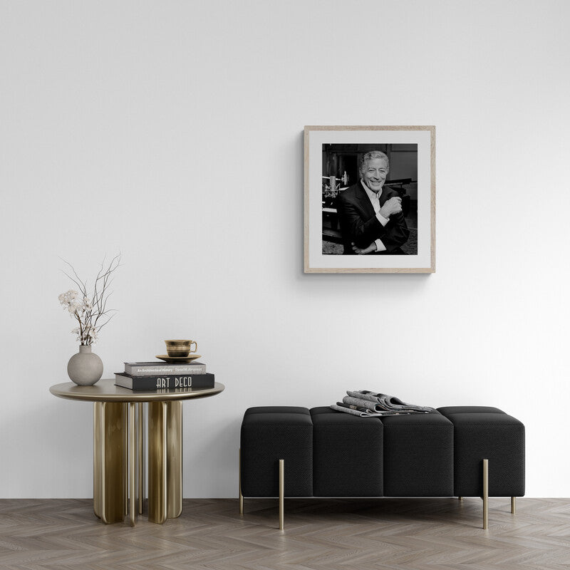 Modern living room with a black sofa, round wooden table, and framed photo on the wall.