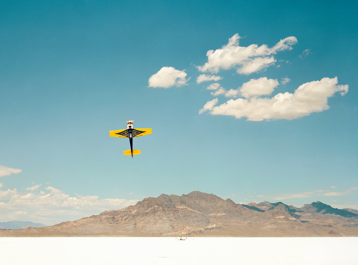 Yellow airplane flying in a clear blue sky with mountains in the background