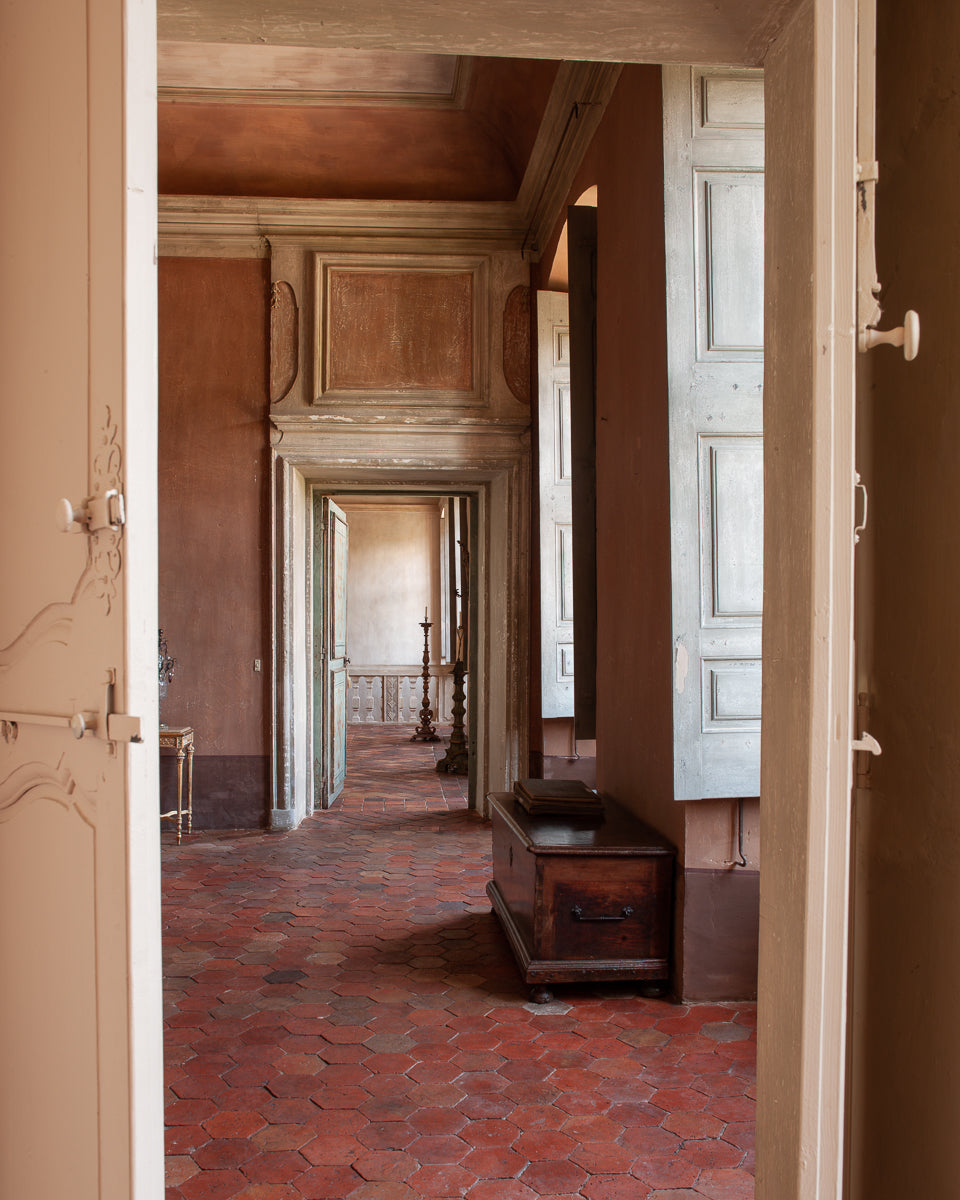 Passageway in an old French castle with a series of wooden doors and a trunk on the floor.