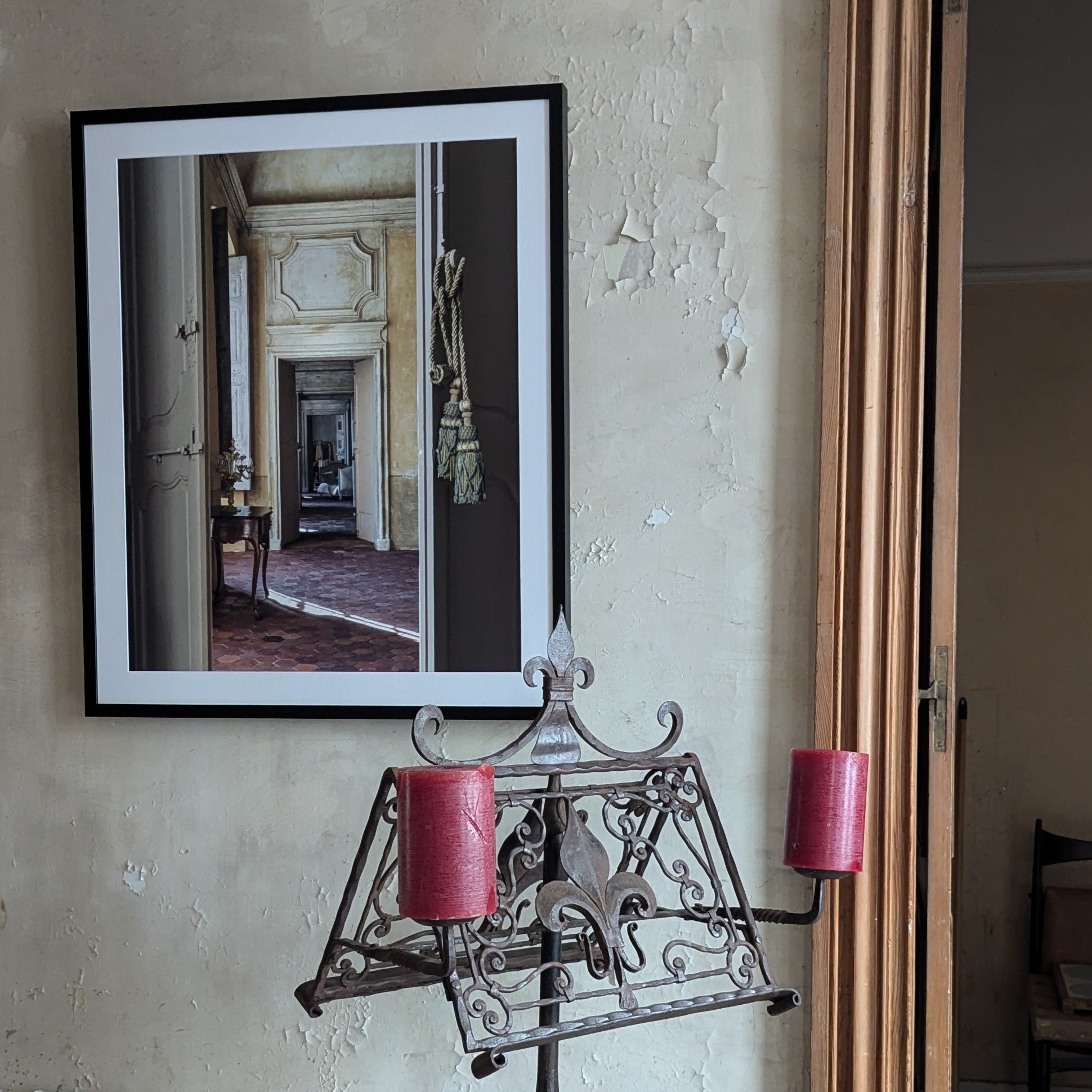 Decorative metal stand with pink candles against a wall with a framed picture.