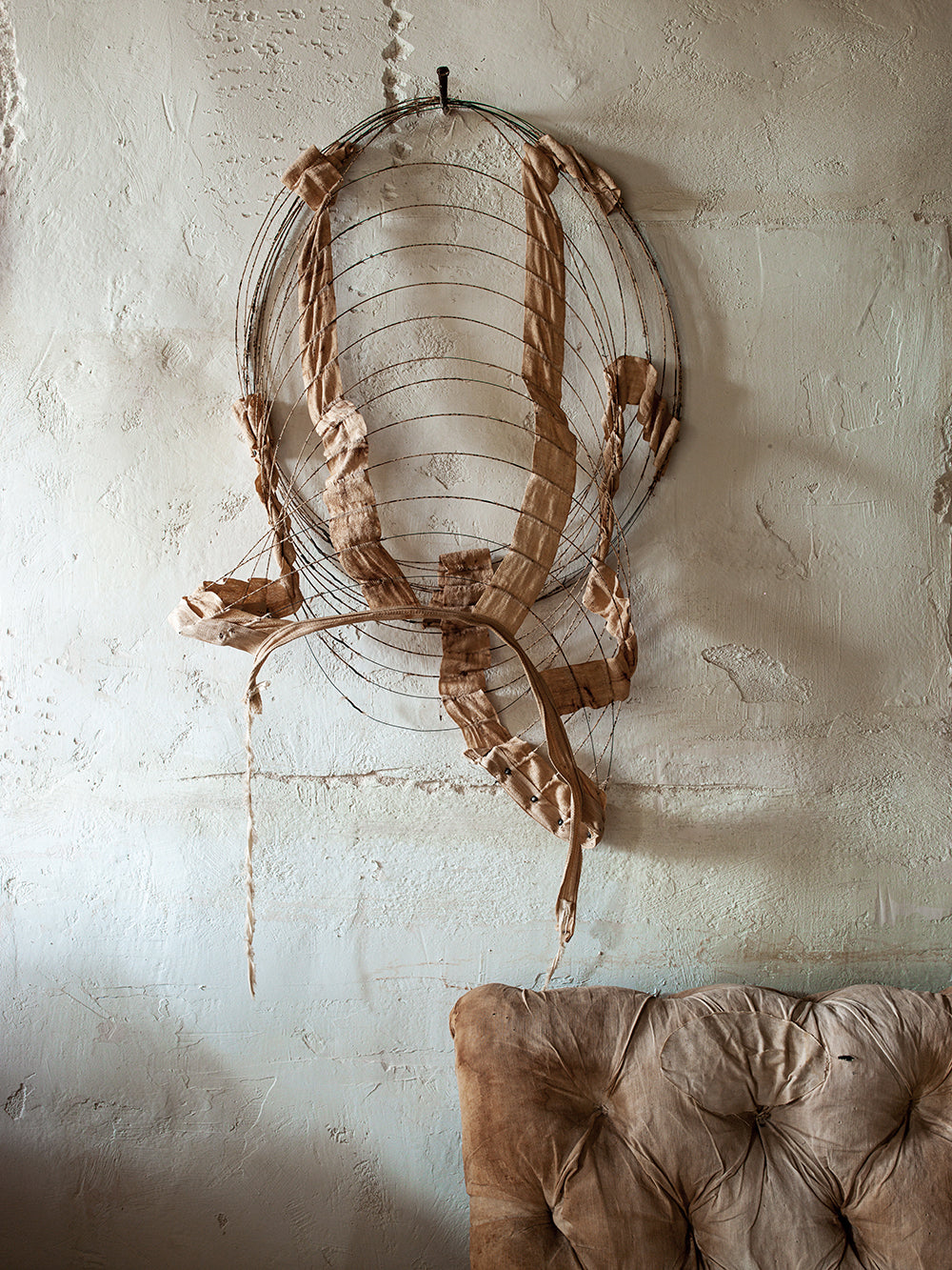 Decorative wall piece made of wire and leather on a textured wall.
