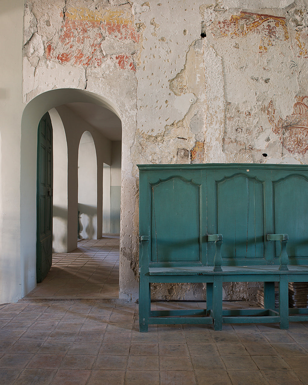 Green wooden bench in an old building with weathered walls and archways.