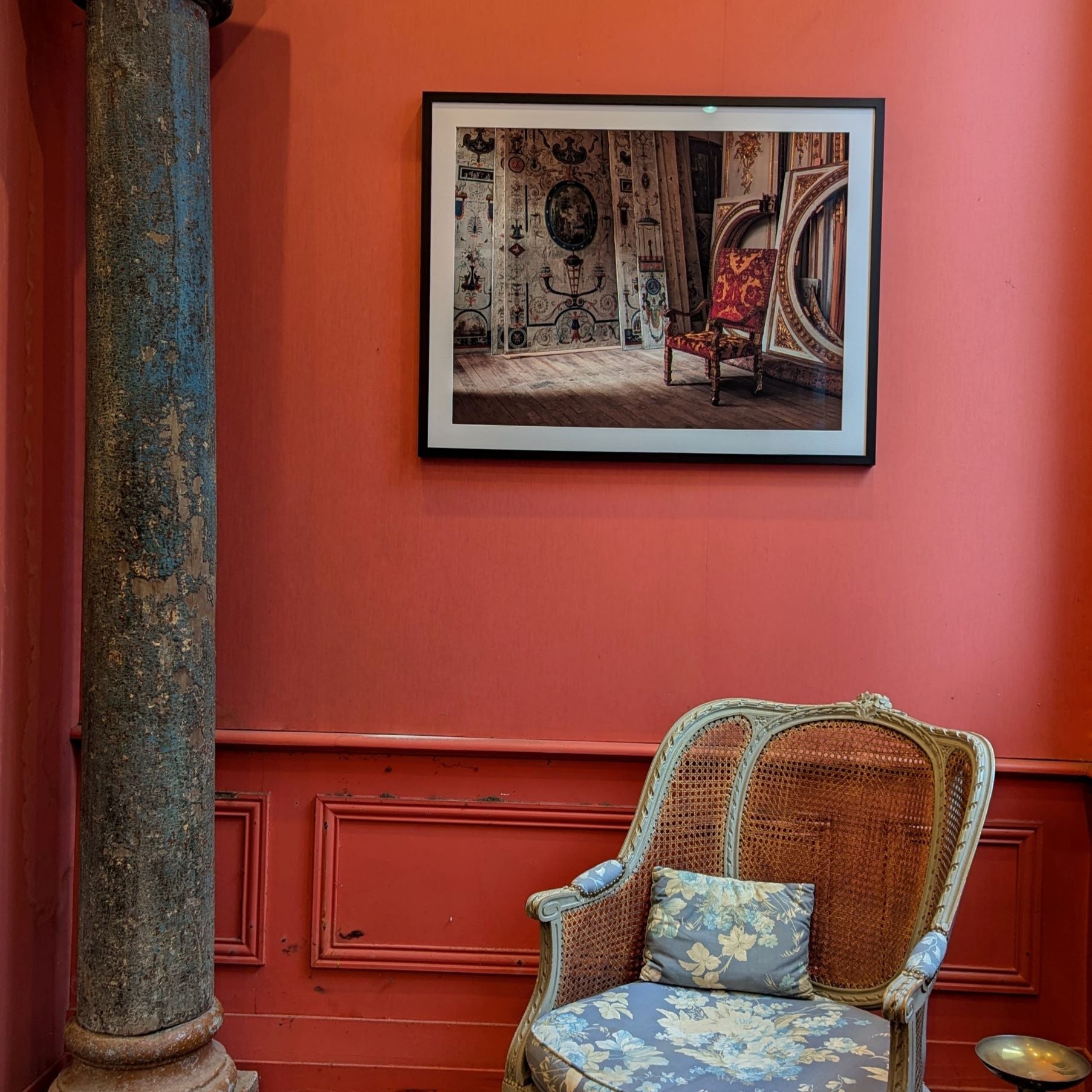 Chair with floral cushions in a room with a framed artwork above it.