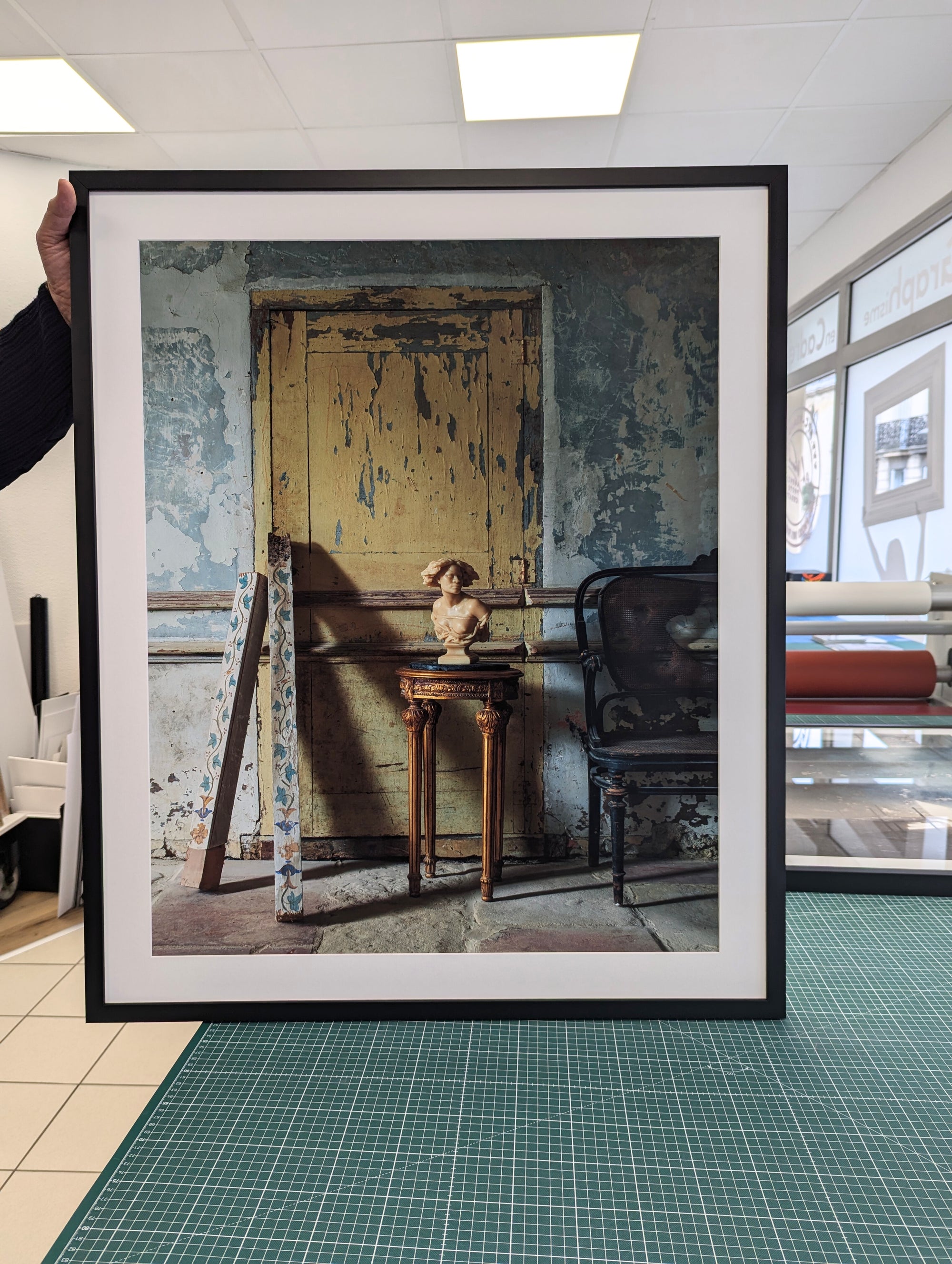 Framed photograph of an interior scene with a distressed wall and chair.