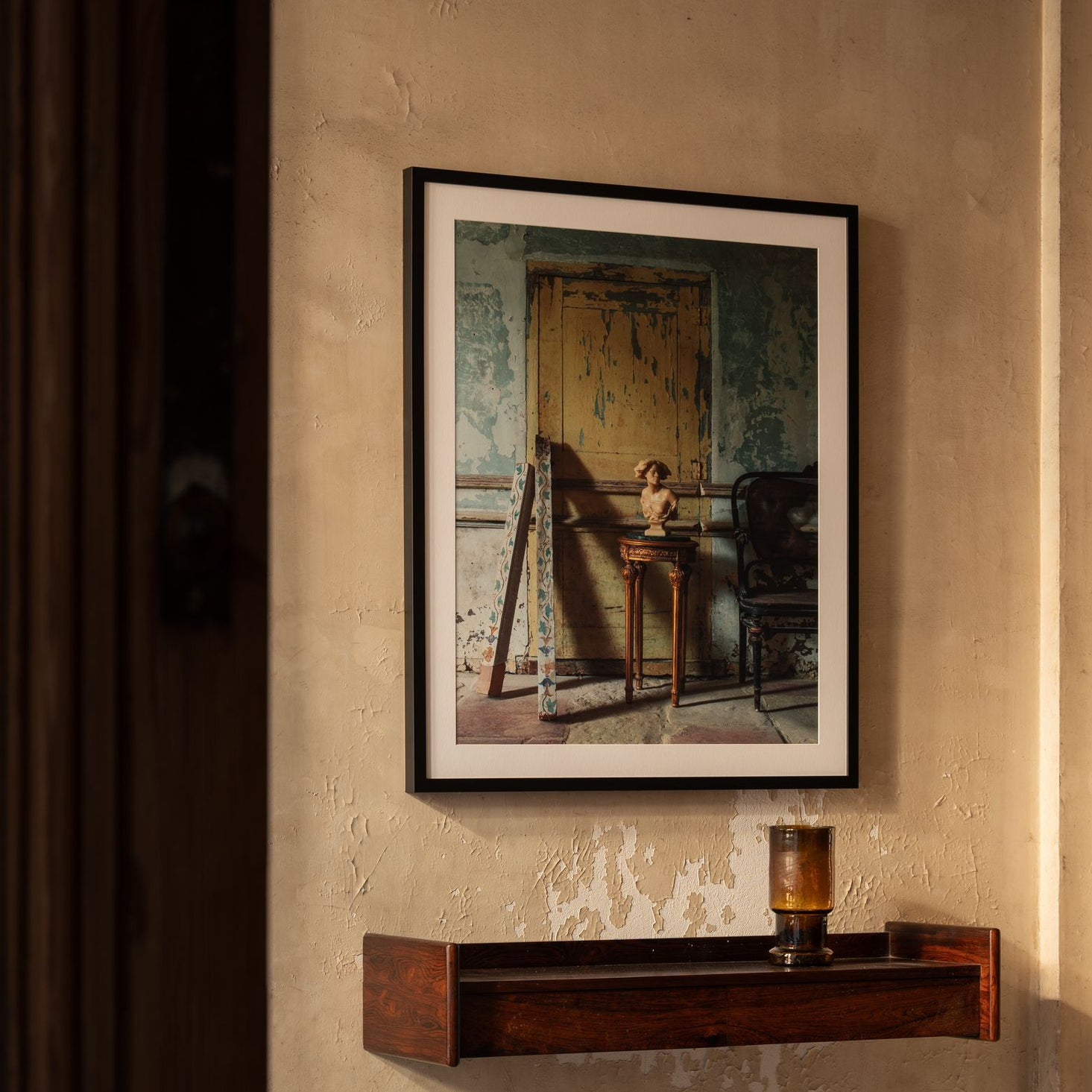 Framed artwork on a textured wall with a wooden shelf below.