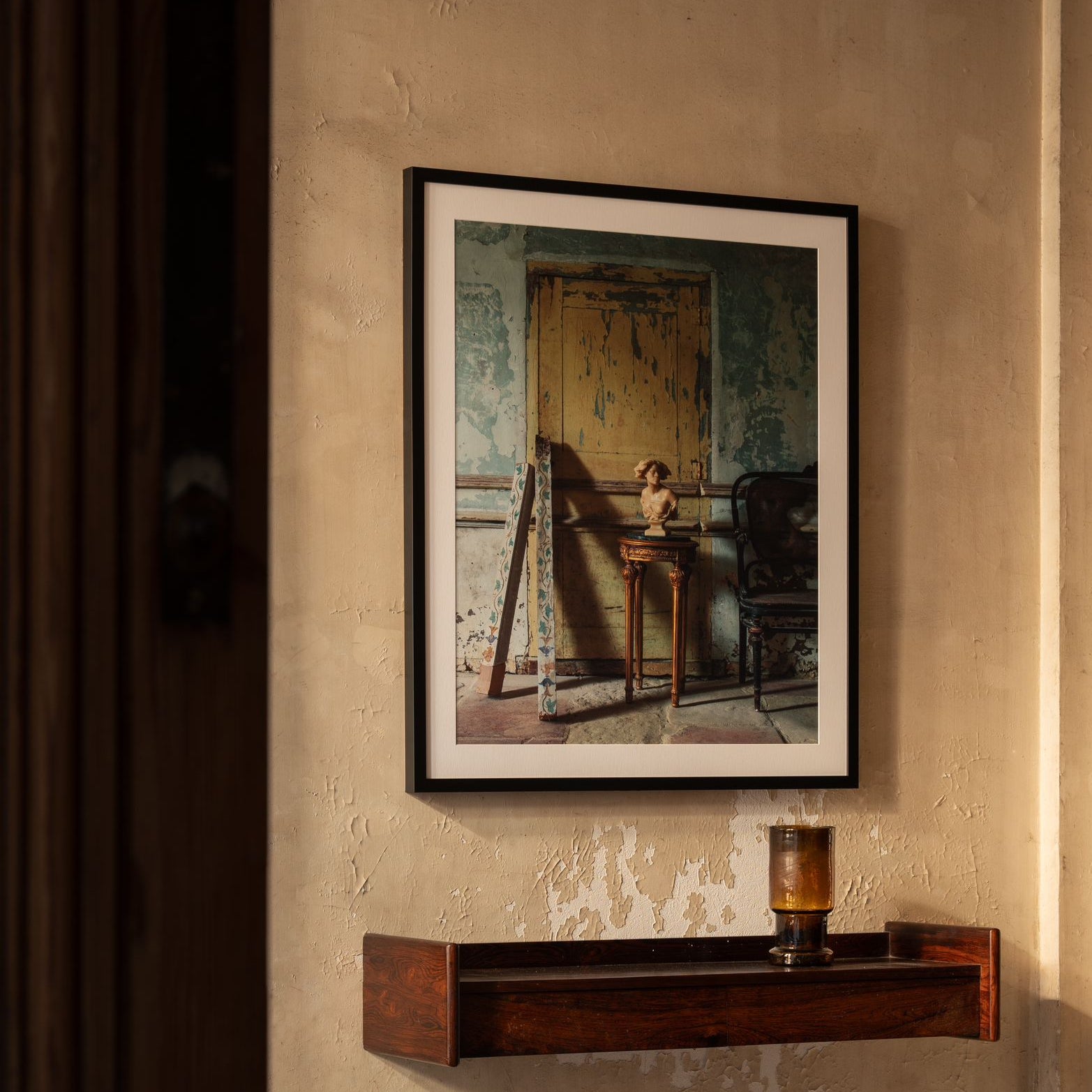 Framed artwork on a textured wall with a wooden shelf below.