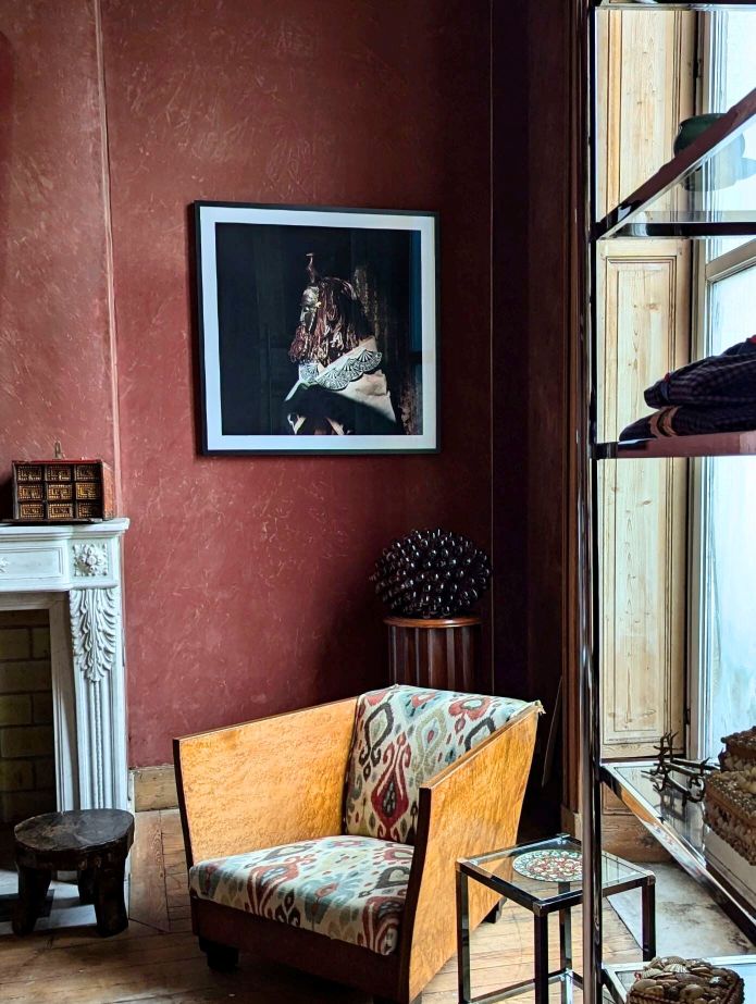 Living room with wooden armchair, framed picture on red wall, and a large window.
