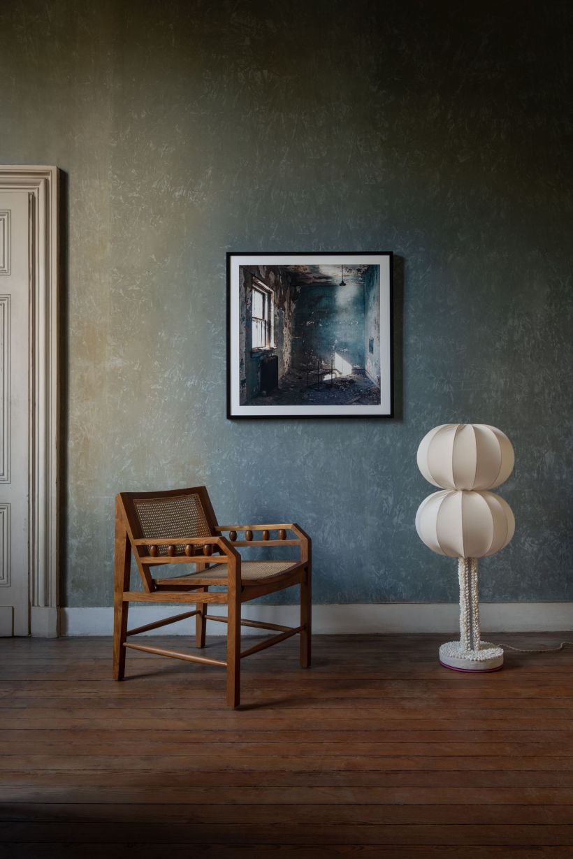 Wooden chair and unique lamp against a textured wall with a framed picture.