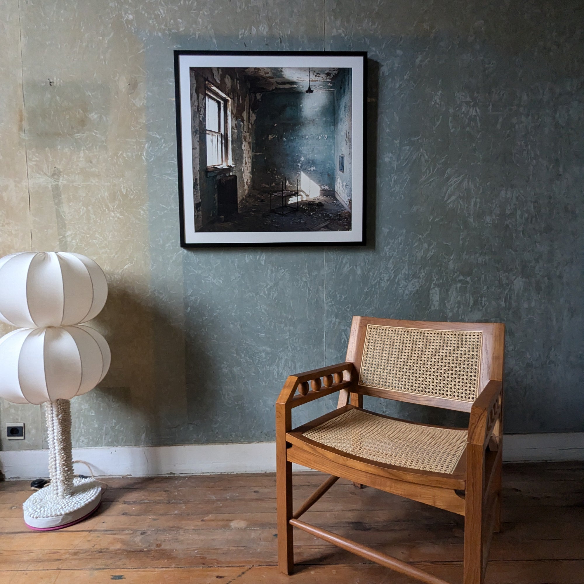 Wooden chair with woven backrest in a room with artwork on the wall, a textured wall and a lamp.