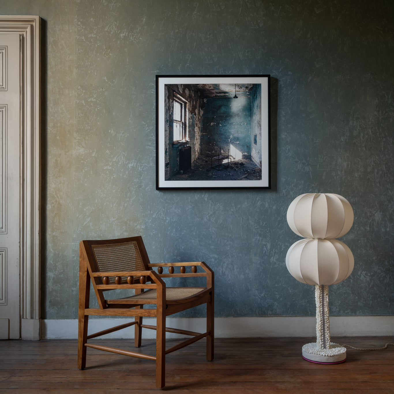 Room interior with a wooden chair, framed artwork, and a unique lamp against a textured wall.