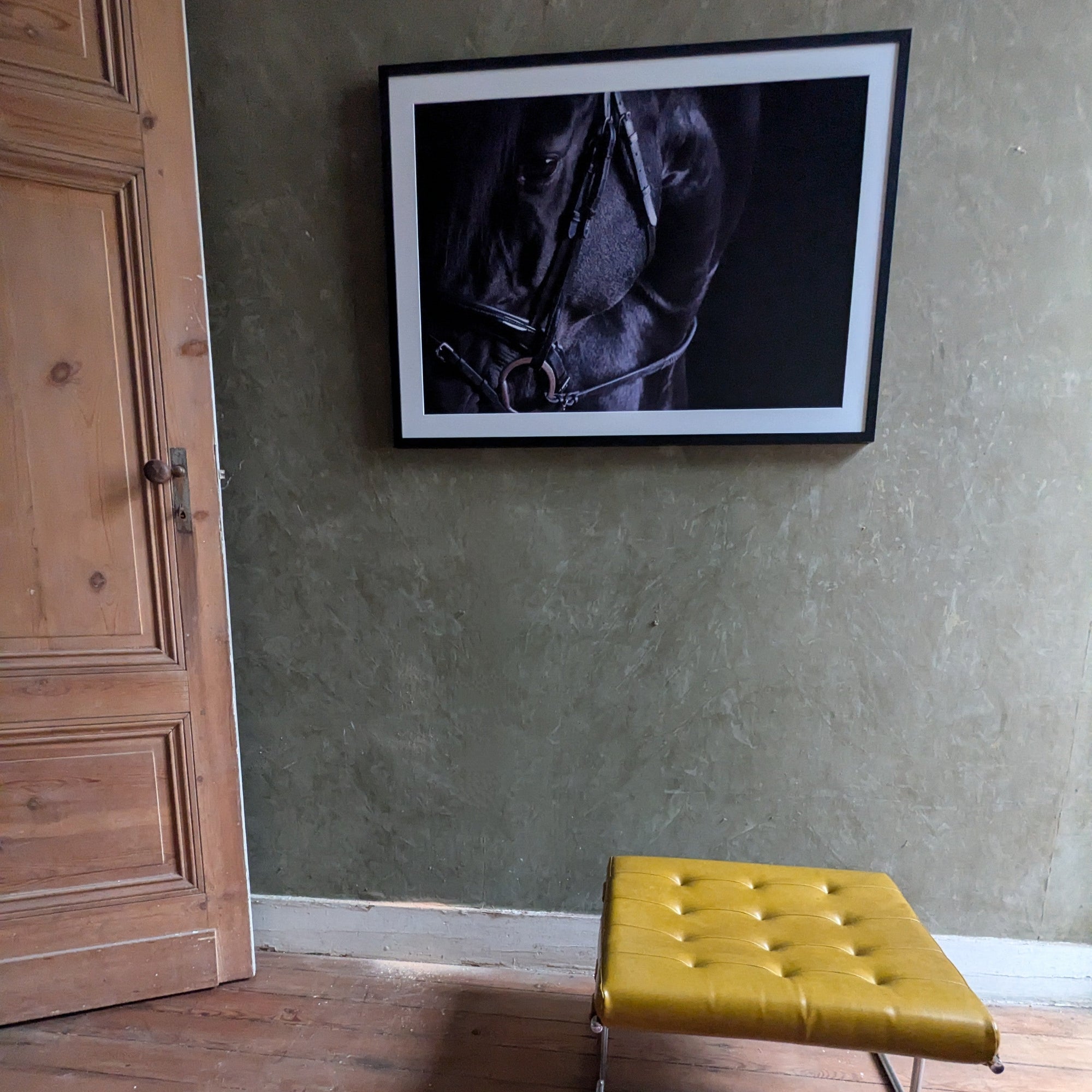 Yellow bench in front of a framed picture on a textured wall.