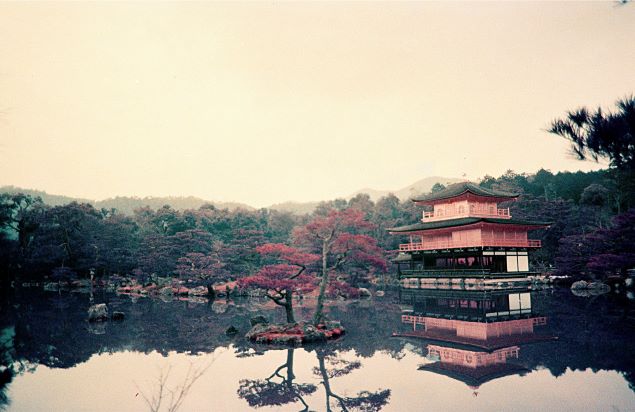 Traditional Japanese building reflected in a pond with trees and mountains in the background