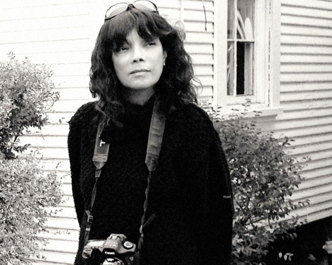 Person holding a camera outdoors in front of a house