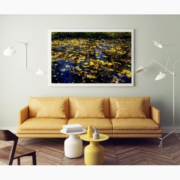 Large print of a pond covered in fallen leaves hanging above a leather couch
