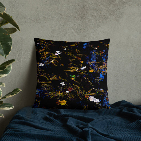 Square pillow with the photograph of a pond covered with flower petals and leaves leaned against a wall