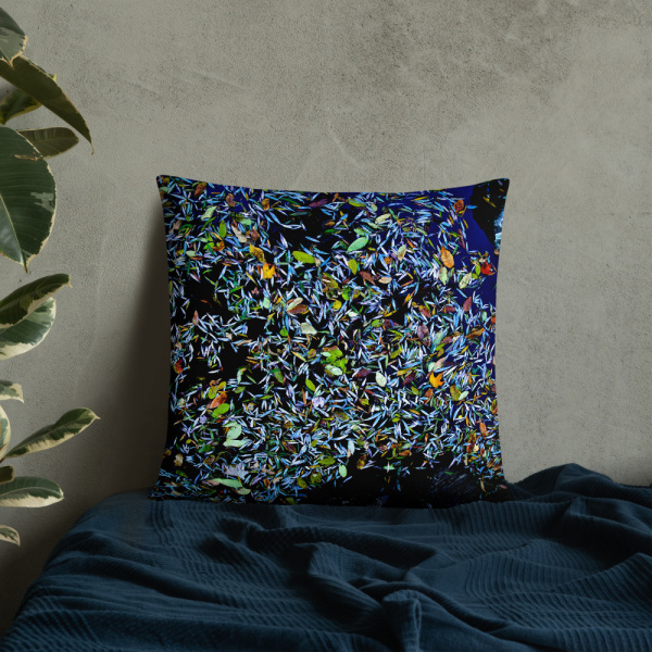Square pillow with a photograph of a pond covered with flower petals leaned against a wall