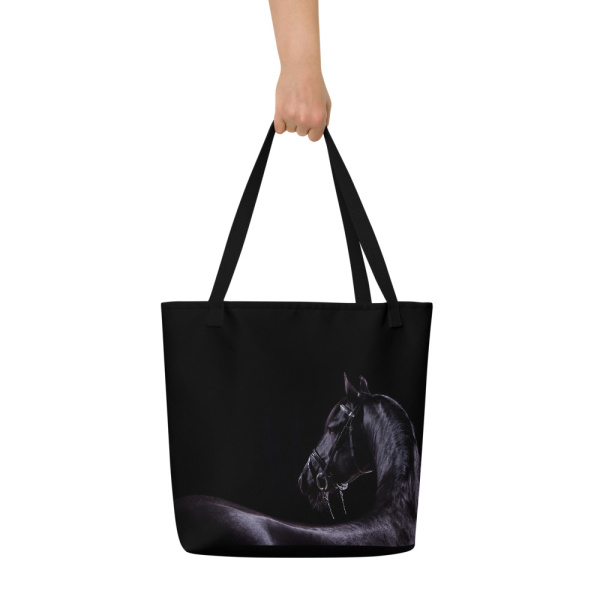 Woman's hand holding a Sideview of a Large black tote bag with the photograph of a black horse on one side