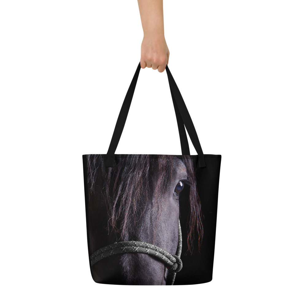 Woman's hand holding a Large black tote bag with a portrait of a black horse in the front