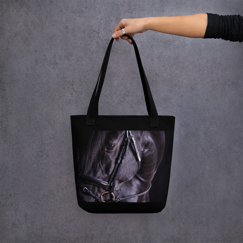 Woman's hand holding a Black tote bag with the portrait of a black horse