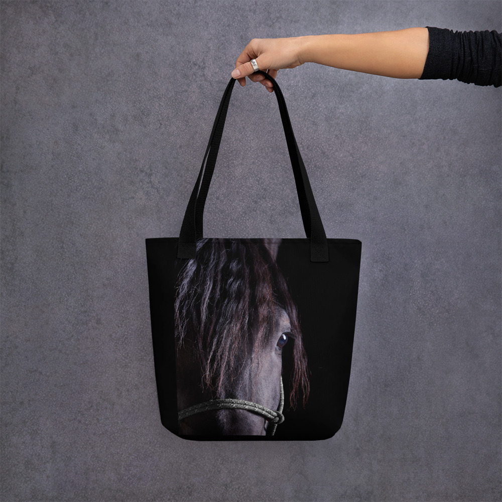 A woman's hand holding a Medium-sized black tote bag with a portrait of a black horse on one side