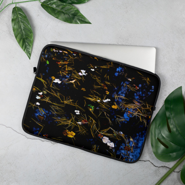On a table, a Laptop case with the photograph of a pond covered in flower petals (black tones)