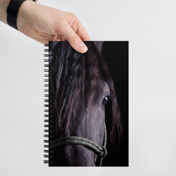 Hand holding a Spiral notebook with a portrait of a black horse
